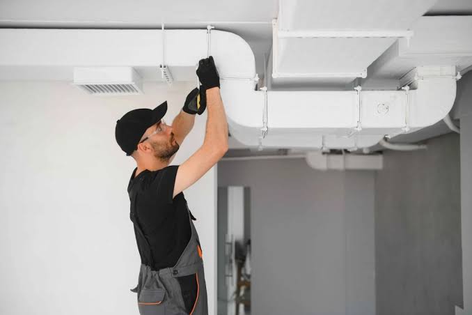 Technician inspecting overhead white ventilation ductwork