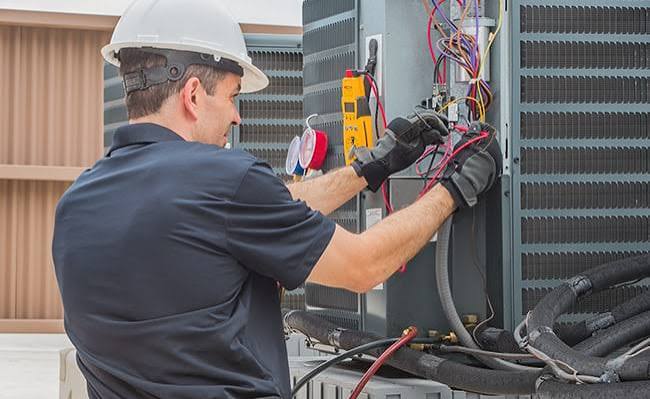 Technician testing wiring and electrical connections in an outdoor HVAC service panel