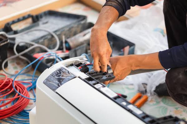 Technician repairing a disassembled indoor air conditioning unit with tools nearby
