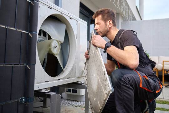 Technician inspecting an outdoor air conditioner with its protective fan grille removed